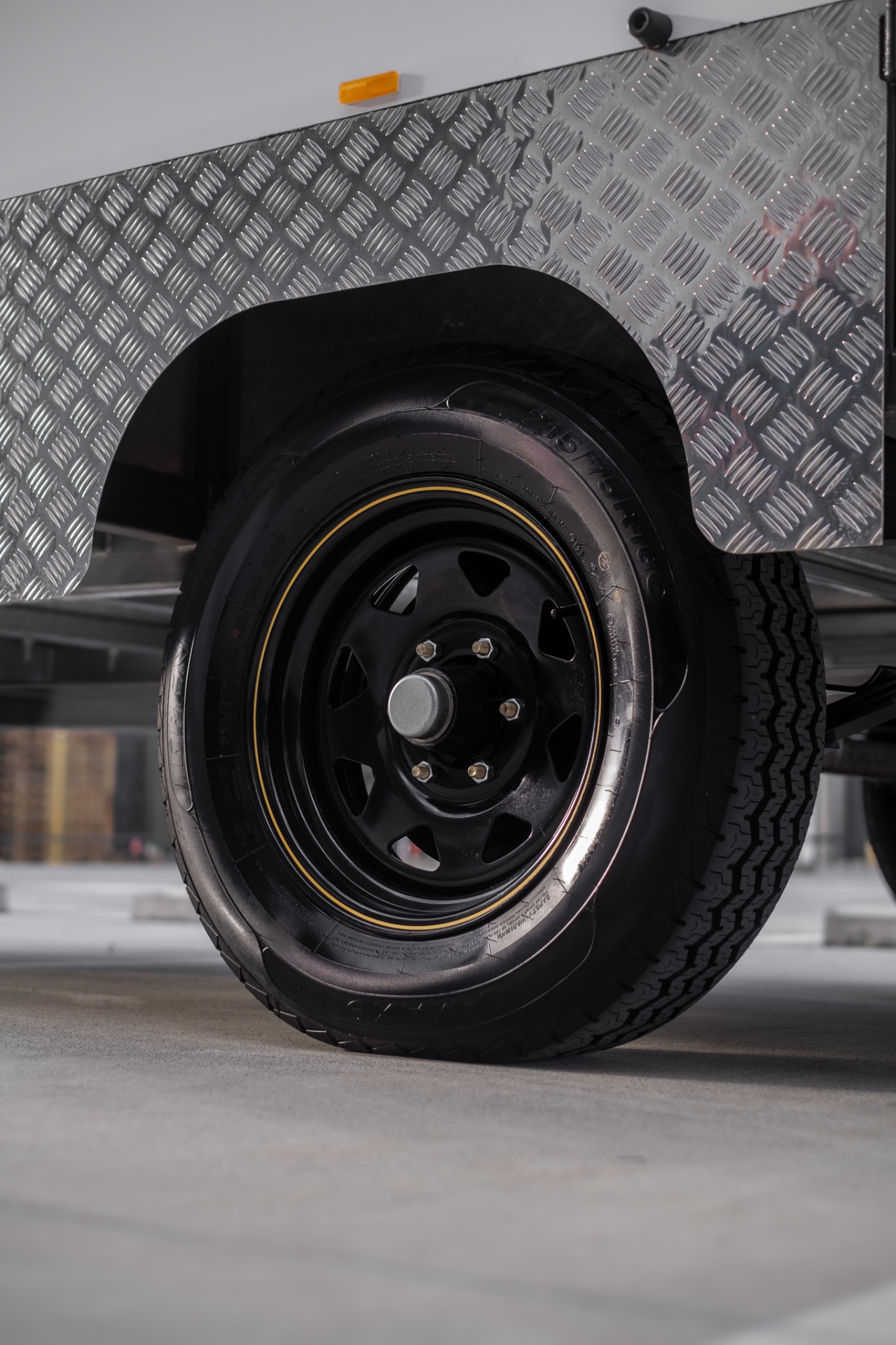 Close-up of the MotoCampers 001 black steel wheel, tyre and checkerplate guard
