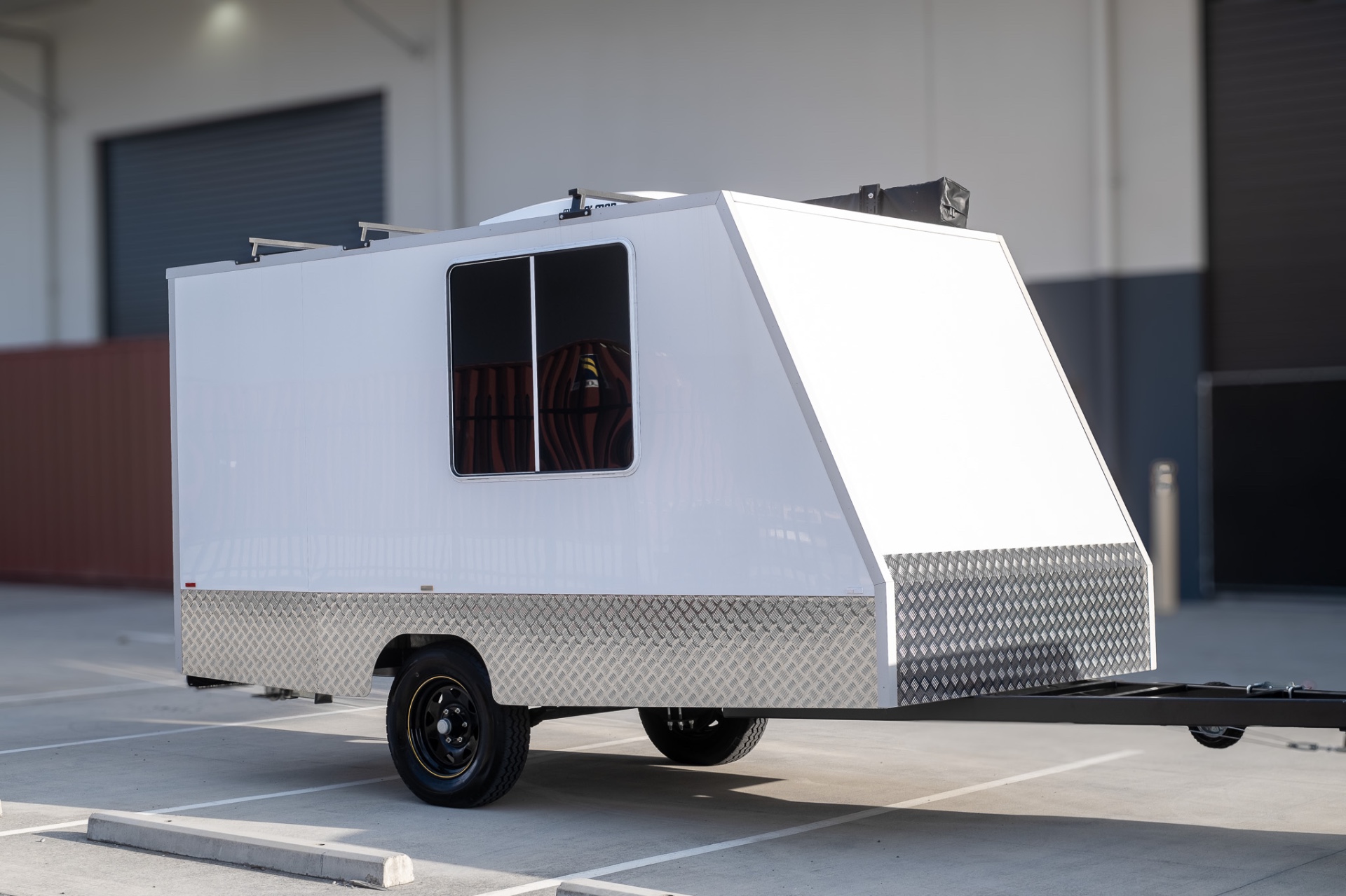 Front three-quarter view of the MotoCampers 001 enclosed trailer with checkerplate lower panels